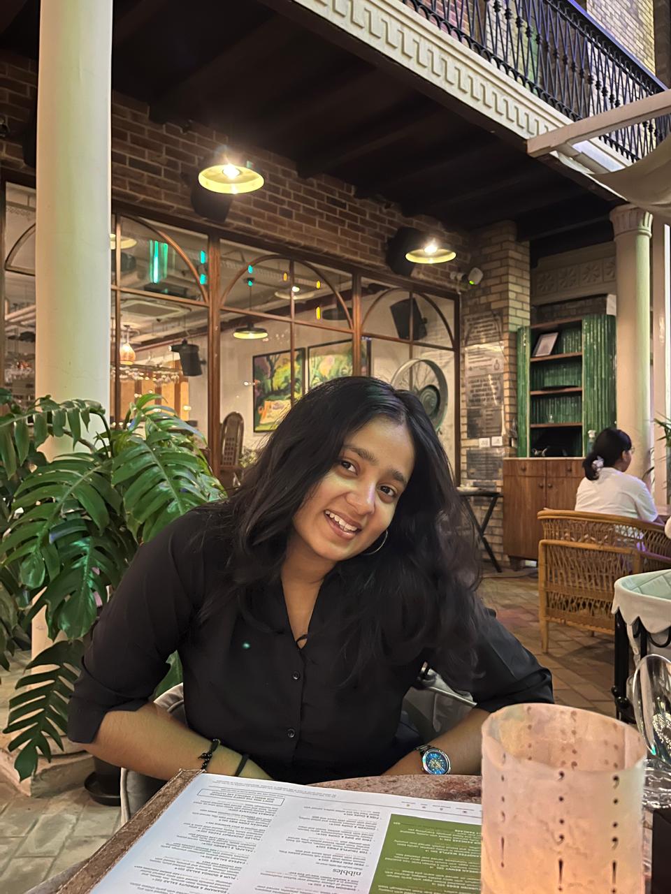 Kanishka Verma smiling warmly at a cafe, wearing a black shirt